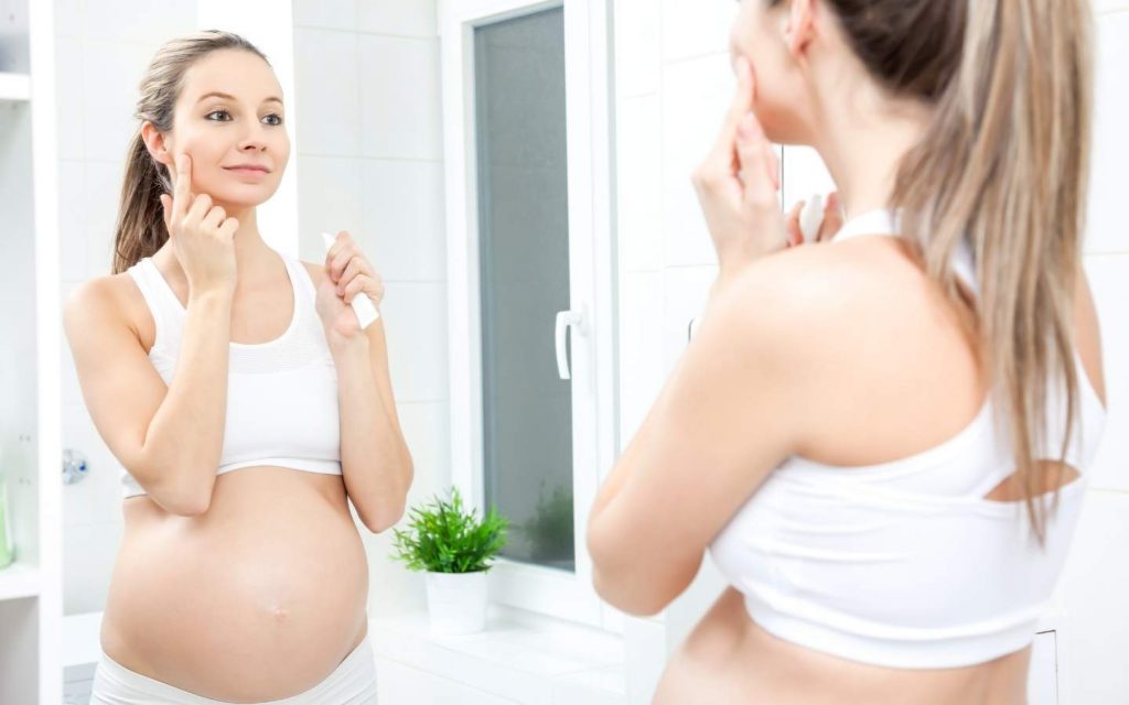 schwangere Frau schaut in den Spiegel und cremt ihr Gesicht ein