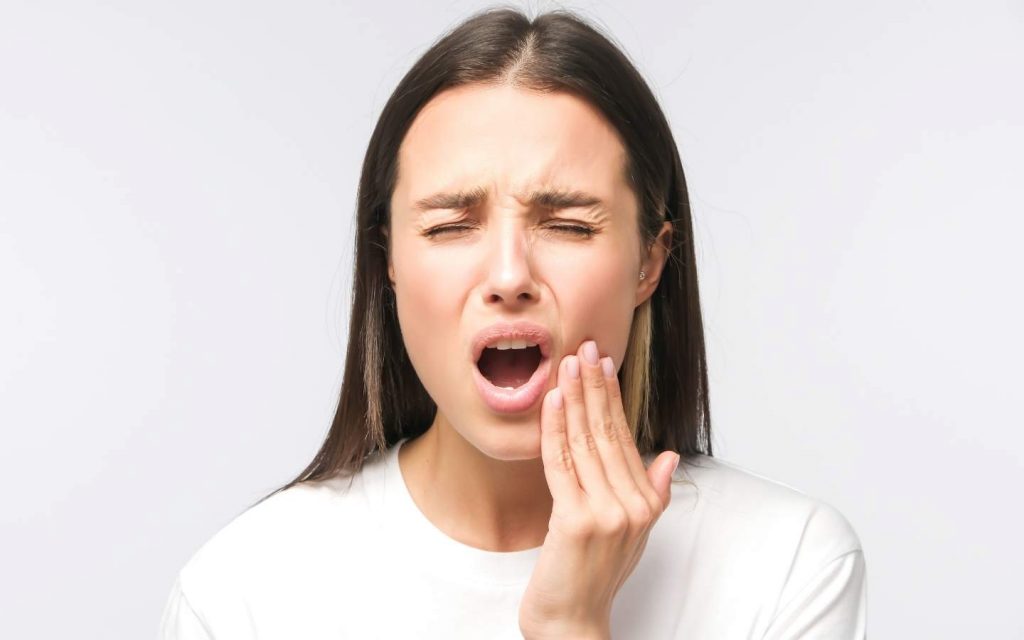 Frau mit Zahnschmerzen fässt sich an die Backe